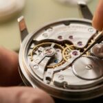 精密な機械式時計のムーブメントを調整する日本人の職人の手元。ゼンマイと歯車の複雑な仕組みが高級感を伝える。